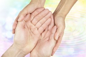 Female hands gently holding male hands in cupped position on a subtle rainbow colored water ripple background fading to white with plenty of copy space